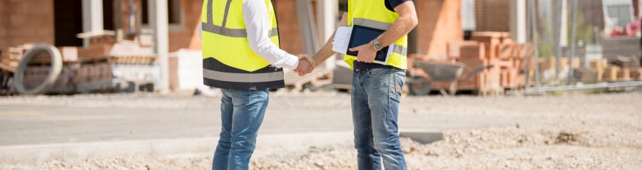 Manager and builder shaking hands on construction site in front of building shell