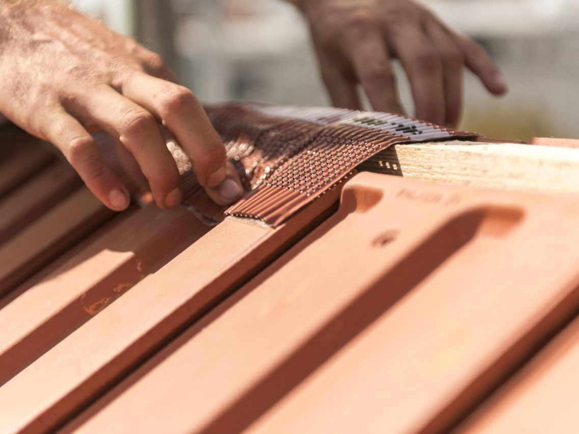 Roofer applying Alu-Grip Rol ridge and hip roll on ridge with bare hands