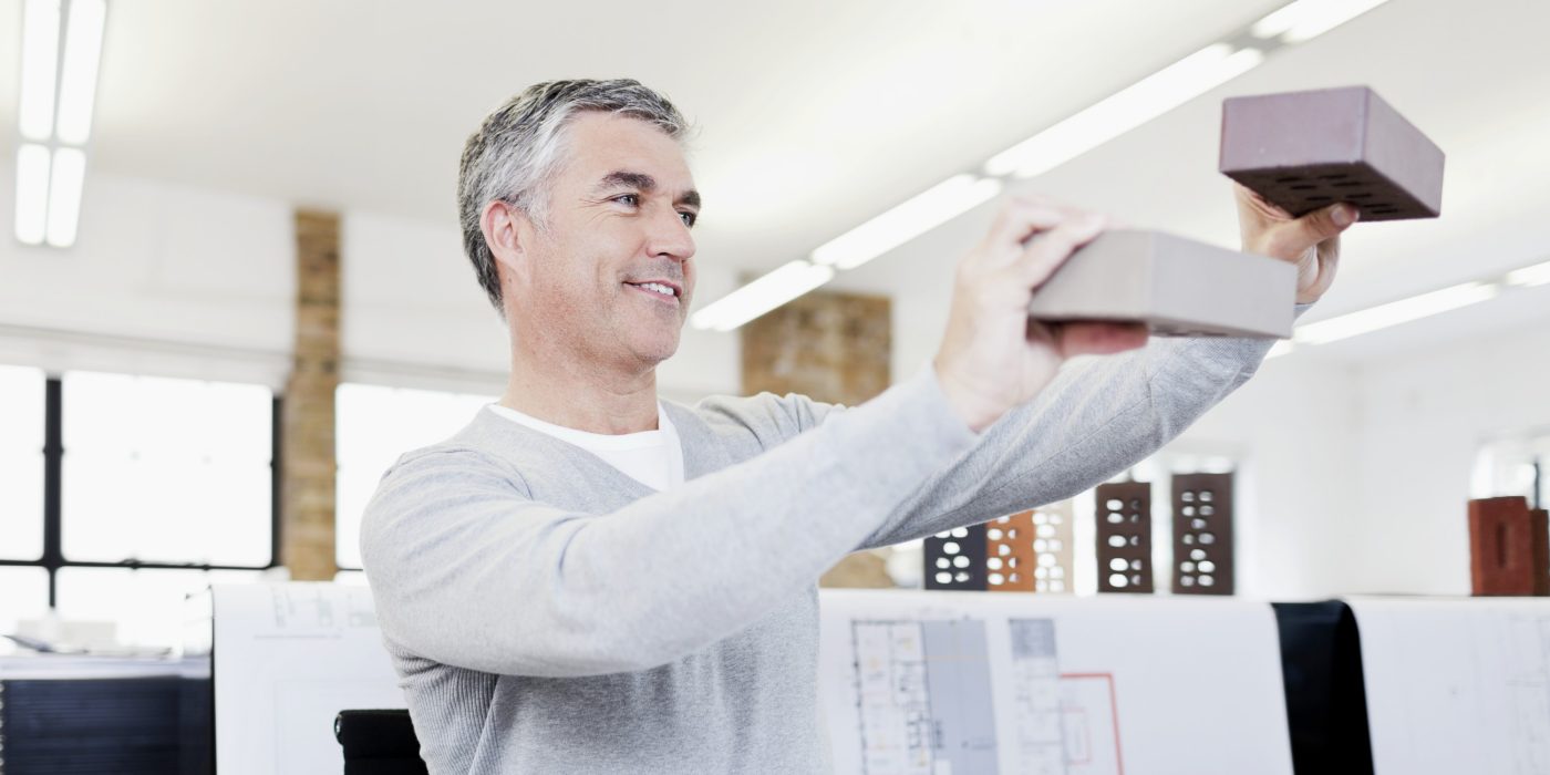 Smiling architect at his office surrounded by blueprints inspecting bricks