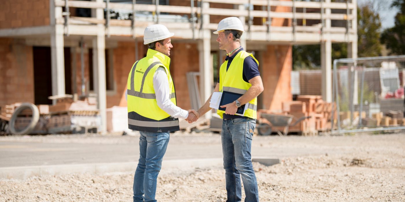 Manager and builder shaking hands on construction site in front of building shell