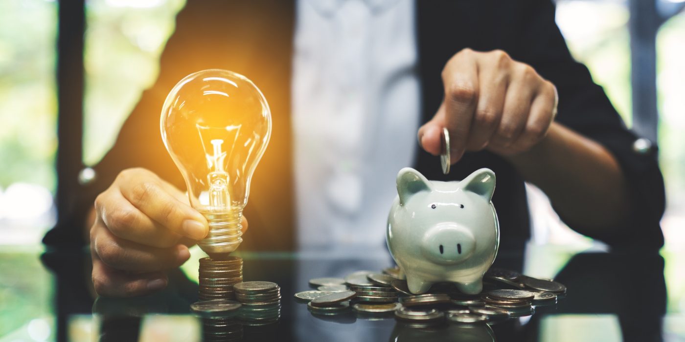 A businesswoman putting coin into piggy bank and a light bulb over coins stack on the table for saving money and financial concept