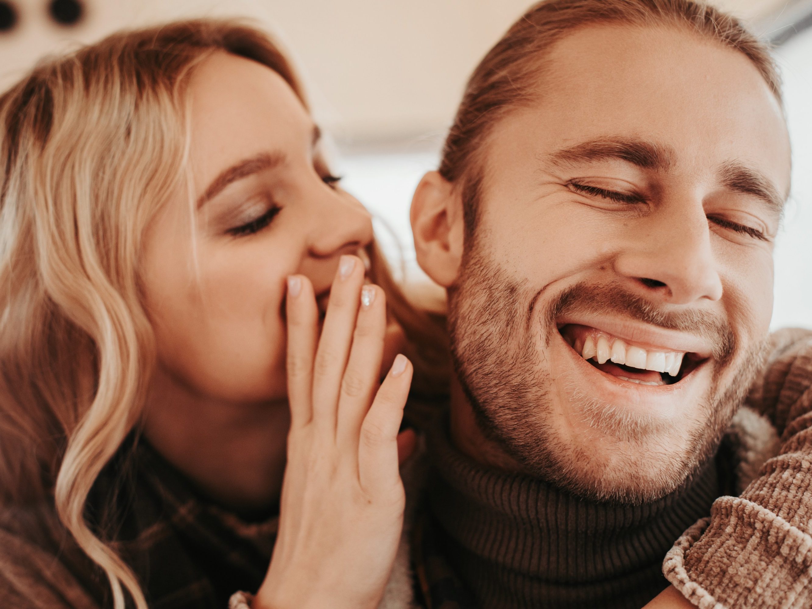 Love is in the air. Close up portrait of happy woman whispering on ear something pleasant to her beloved laughing hipster man while embracing him