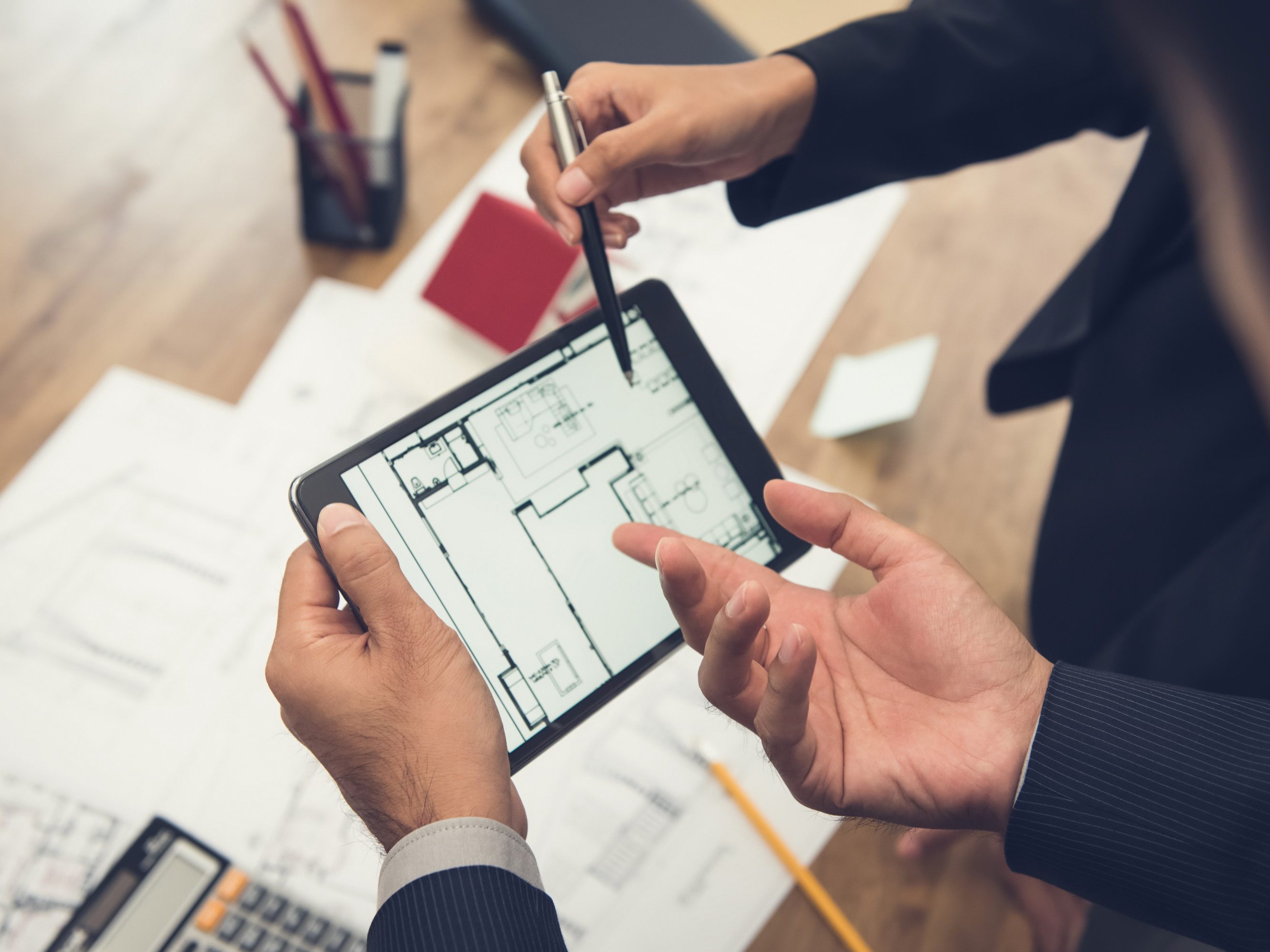 Real estate agent with client or architect team discussing a housing model and its blueprints digitally using a tablet computer