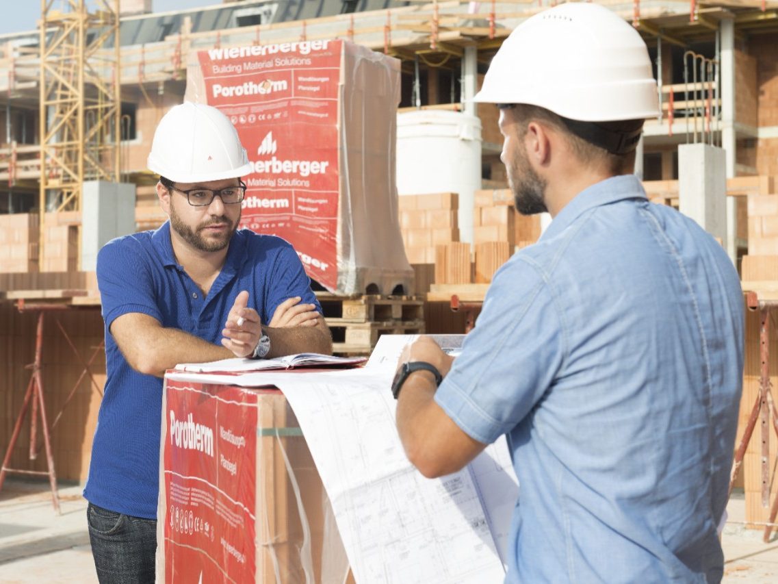 Building professionals talking on contruction site leaning on foil wrapped palette of brick blocks