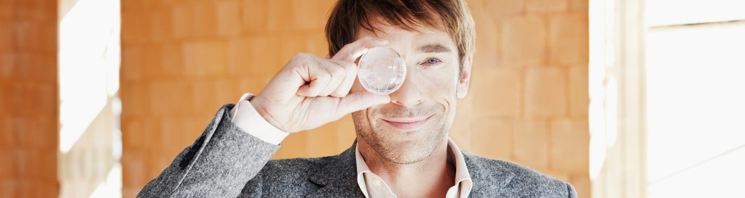 Smiling man looking through a glass globe facing camera