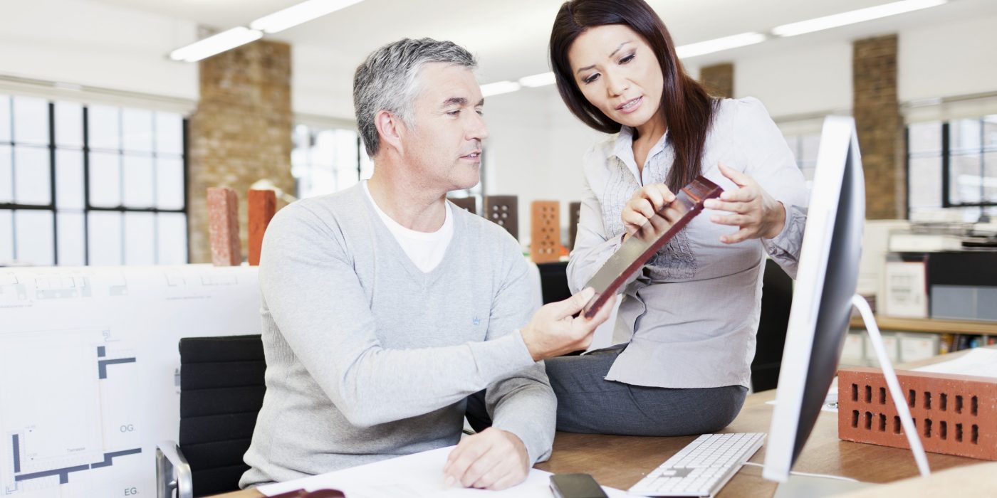 Male and female architect at office desk in their studio examining the surface of a clay roof tile