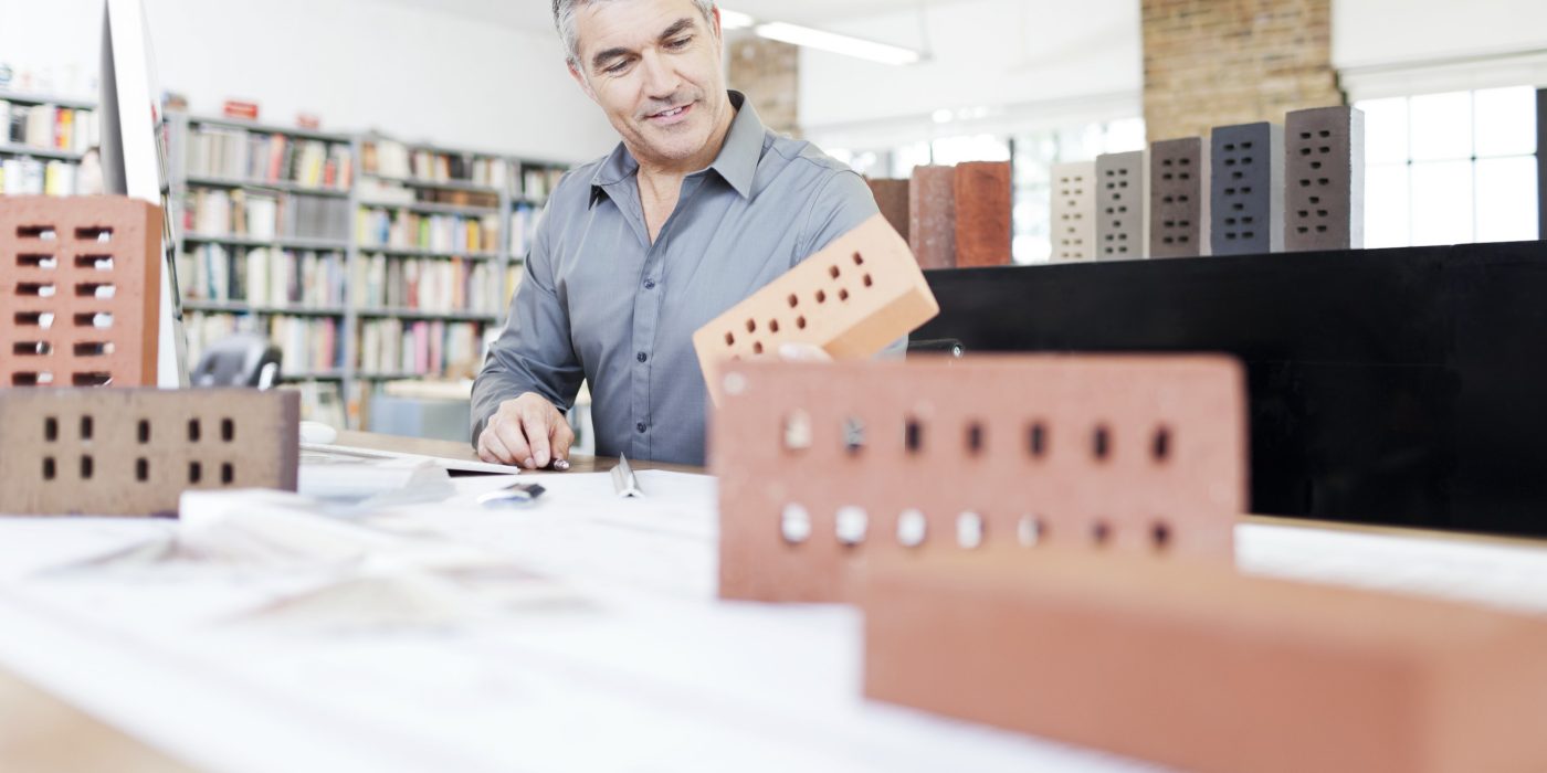 Architect at his office sitting at desk with blueprint surrounded by bricks