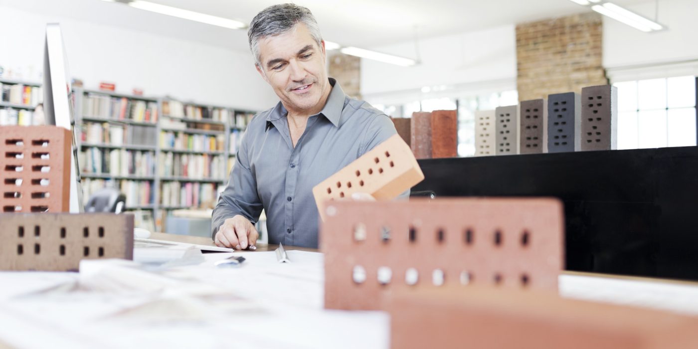 Architect at his office sitting at desk with blueprint surrounded by bricks