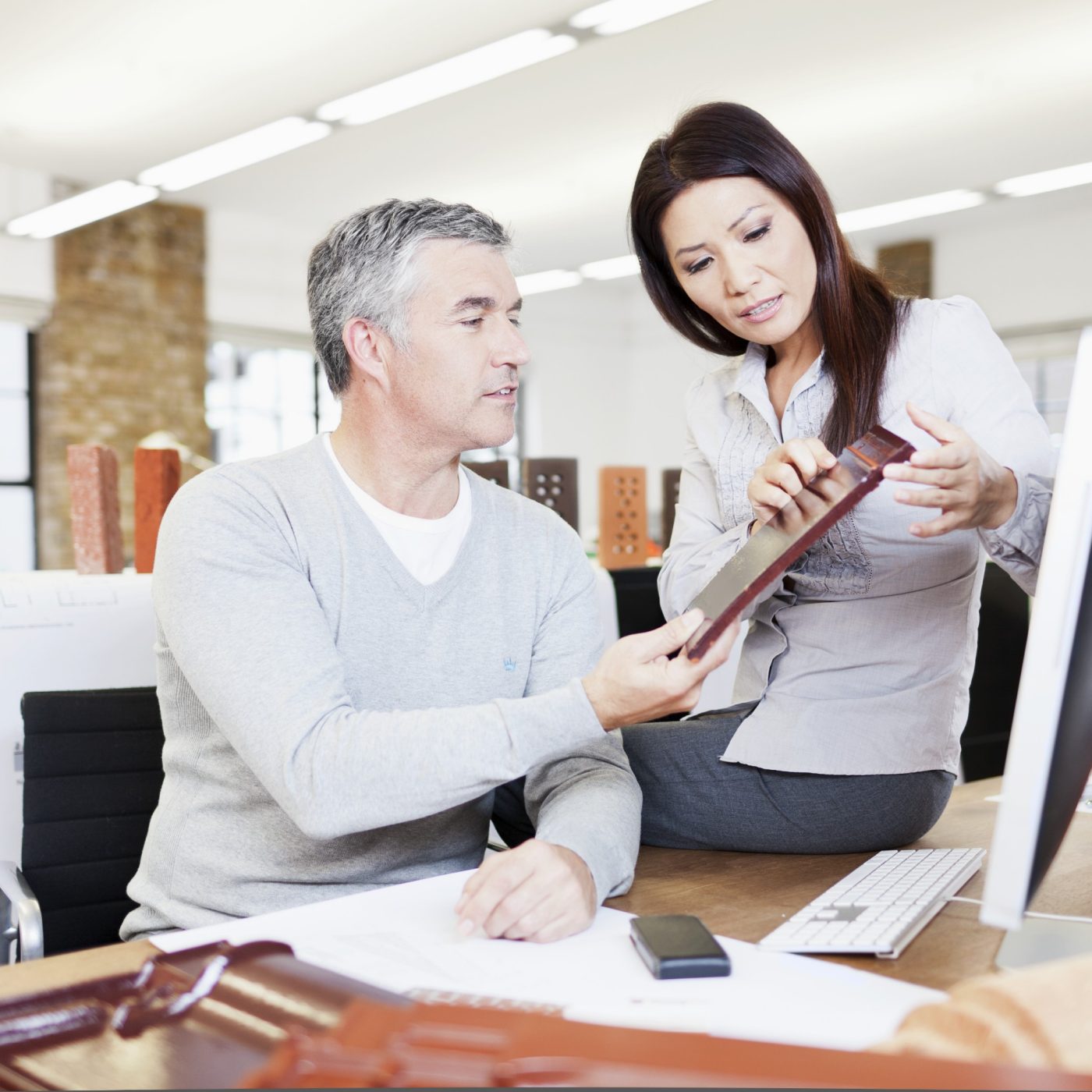 Male and female architect at office desk in their studio examining the surface of a clay roof tile