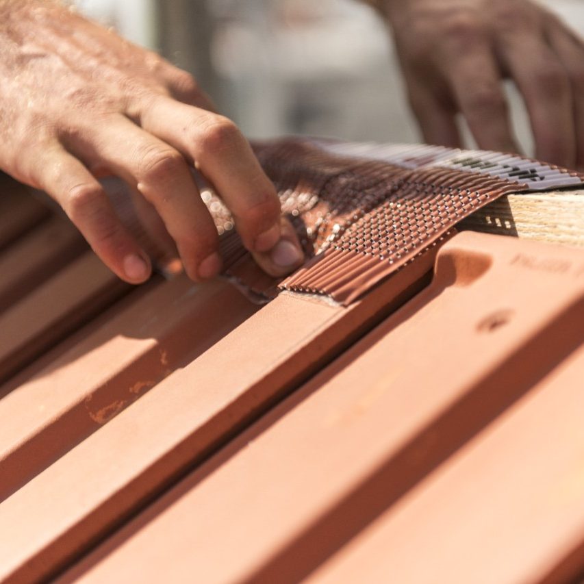 Roofer applying Alu-Grip Rol ridge and hip roll on ridge with bare hands