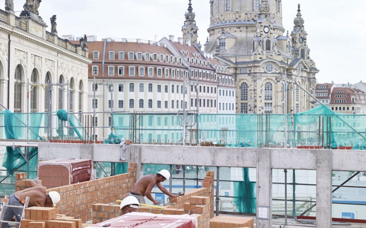 Construction workers are working on the building. In the background you can see apartments and a tower. /  Poroton-S9-MW  /  Poroton-Schallschutzziegel Mz 3DF-2,0
