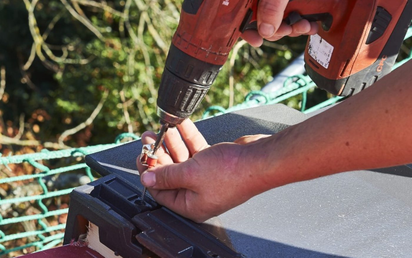 Close-up of a roofer screwing with a cordless drill