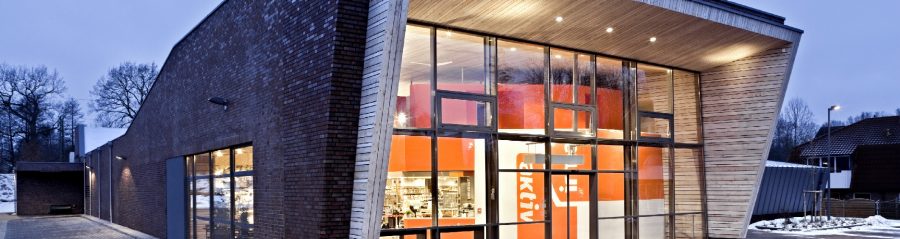 Entrance area of a supermarket in one evening. The market is illuminated from the inside and you can see the surrounding area. There is also a zebra crossing, Bristol, englischblaubraun, rustikal