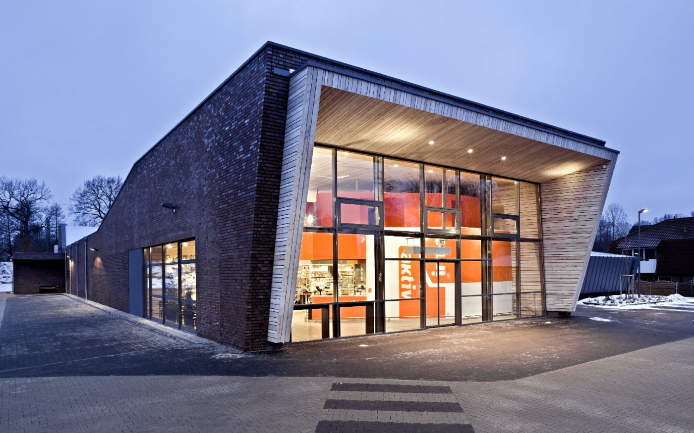 Entrance area of a supermarket in one evening. The market is illuminated from the inside and you can see the surrounding area. There is also a zebra crossing, Bristol, englischblaubraun, rustikal