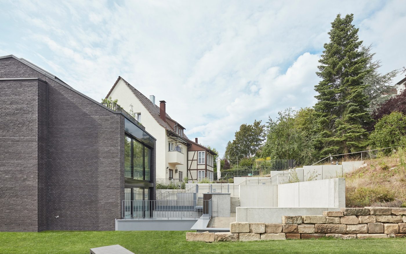 Aus dieser Perspektive unsichtbar ist das großzügige, in den Hang hineinragende Erdgeschoss. Kontrastreich und doch harmonisch fügt sich der moderne Bau in die Umgebung ein.