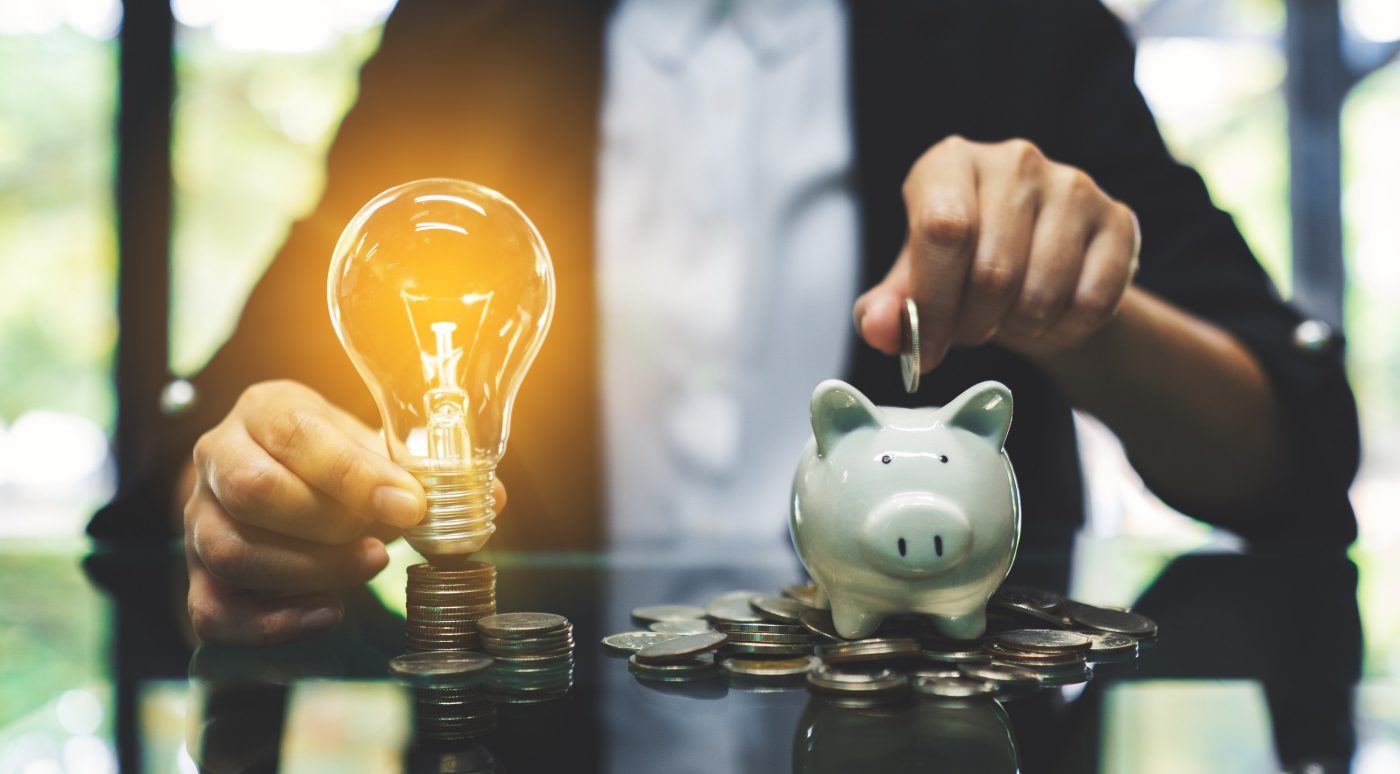 A businesswoman putting coin into piggy bank and a light bulb over coins stack on the table for saving money and financial concept