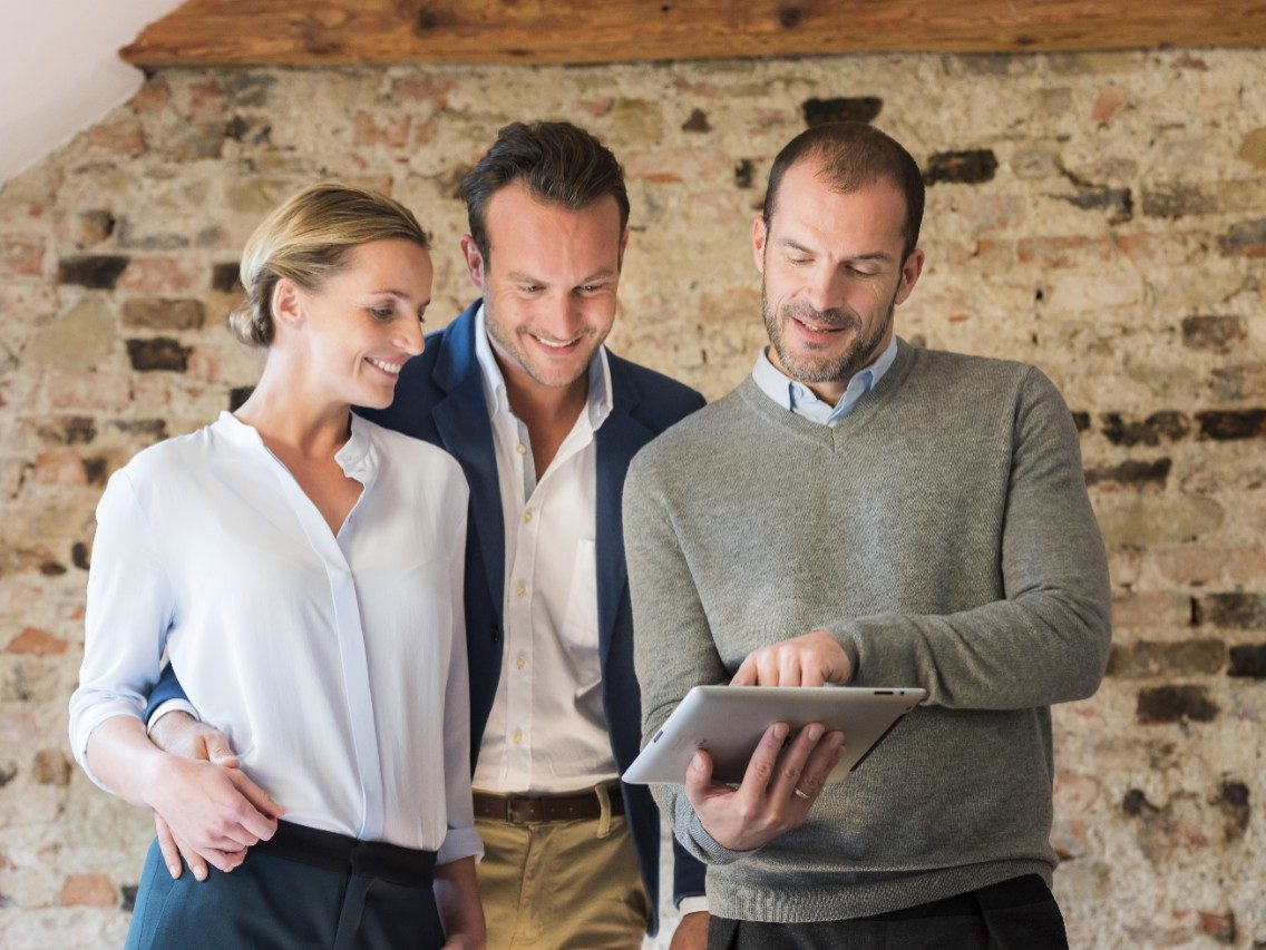 Architect presents project to couple on tablet in front of old brick wall 