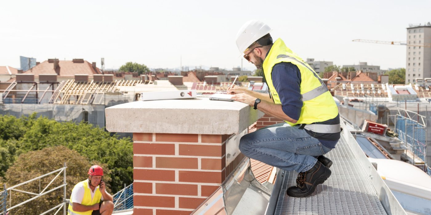 Workers on roof builder checking chimney taking notes