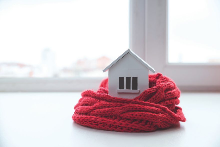 house in winter - heating system concept and cold snowy weather with model of a house wearing a knitted cap.