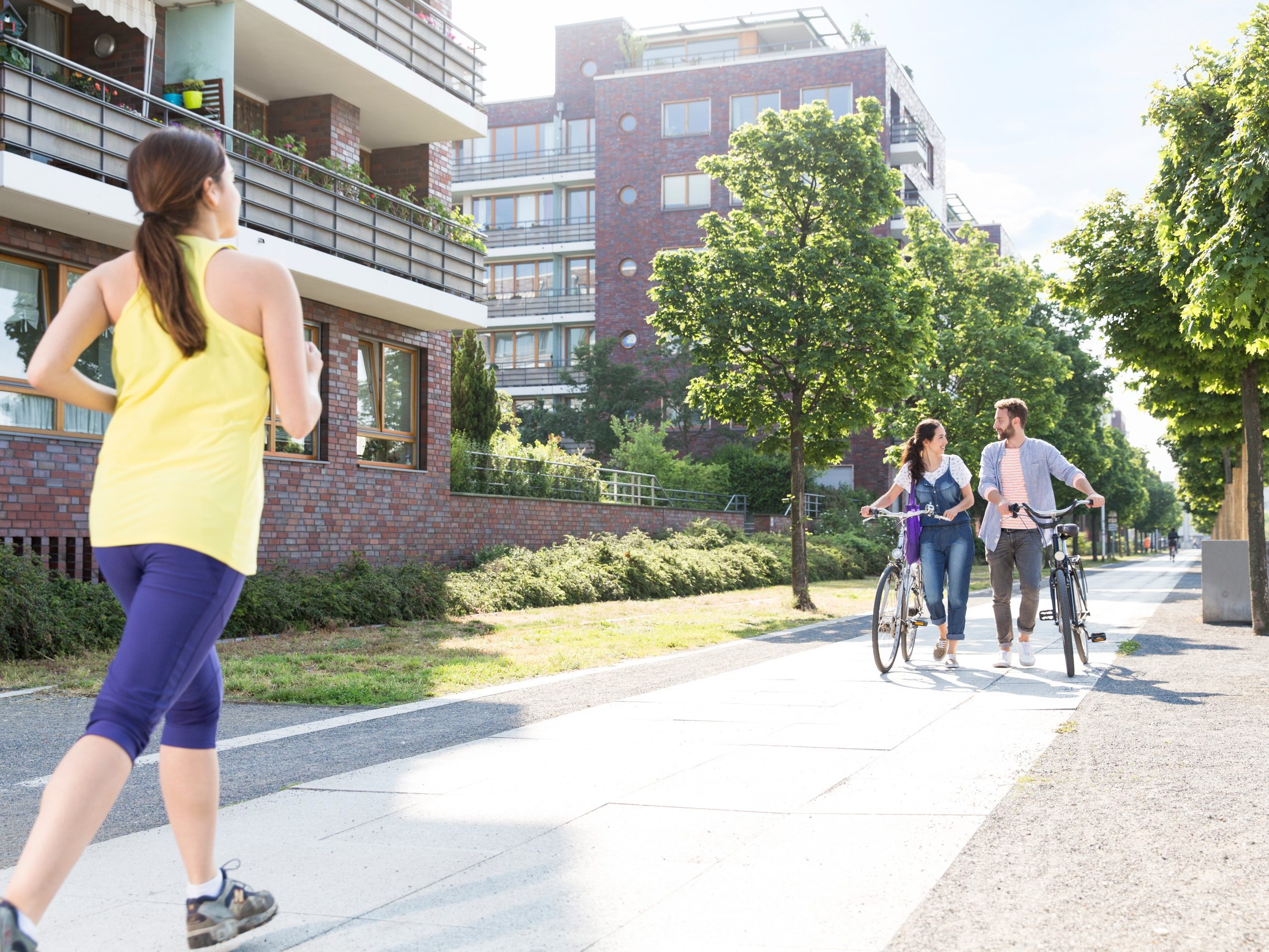Couple pushing bicycles and woman jogging in a newly built housing estate